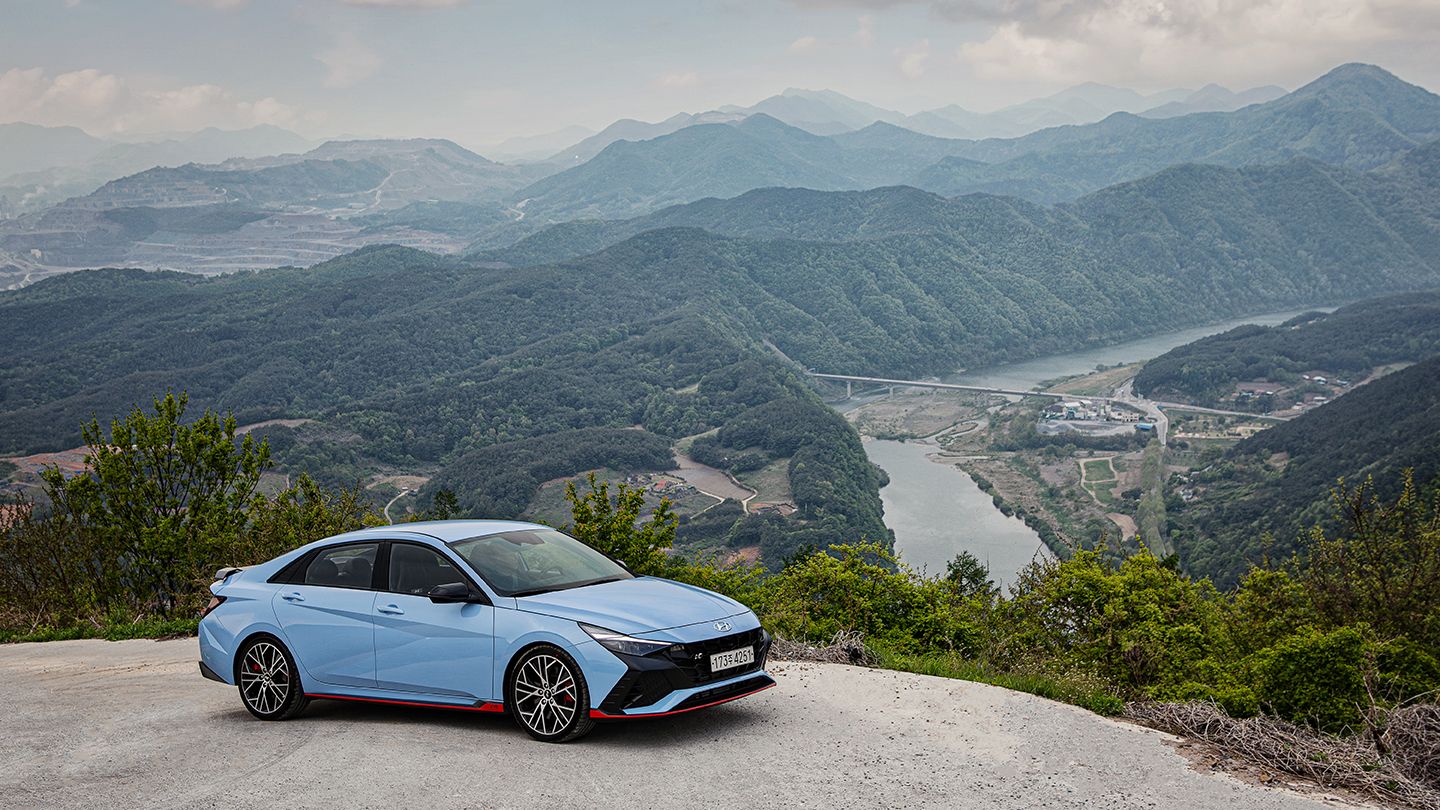 A mountain background is visible behind the Elantra N parked on the right side.