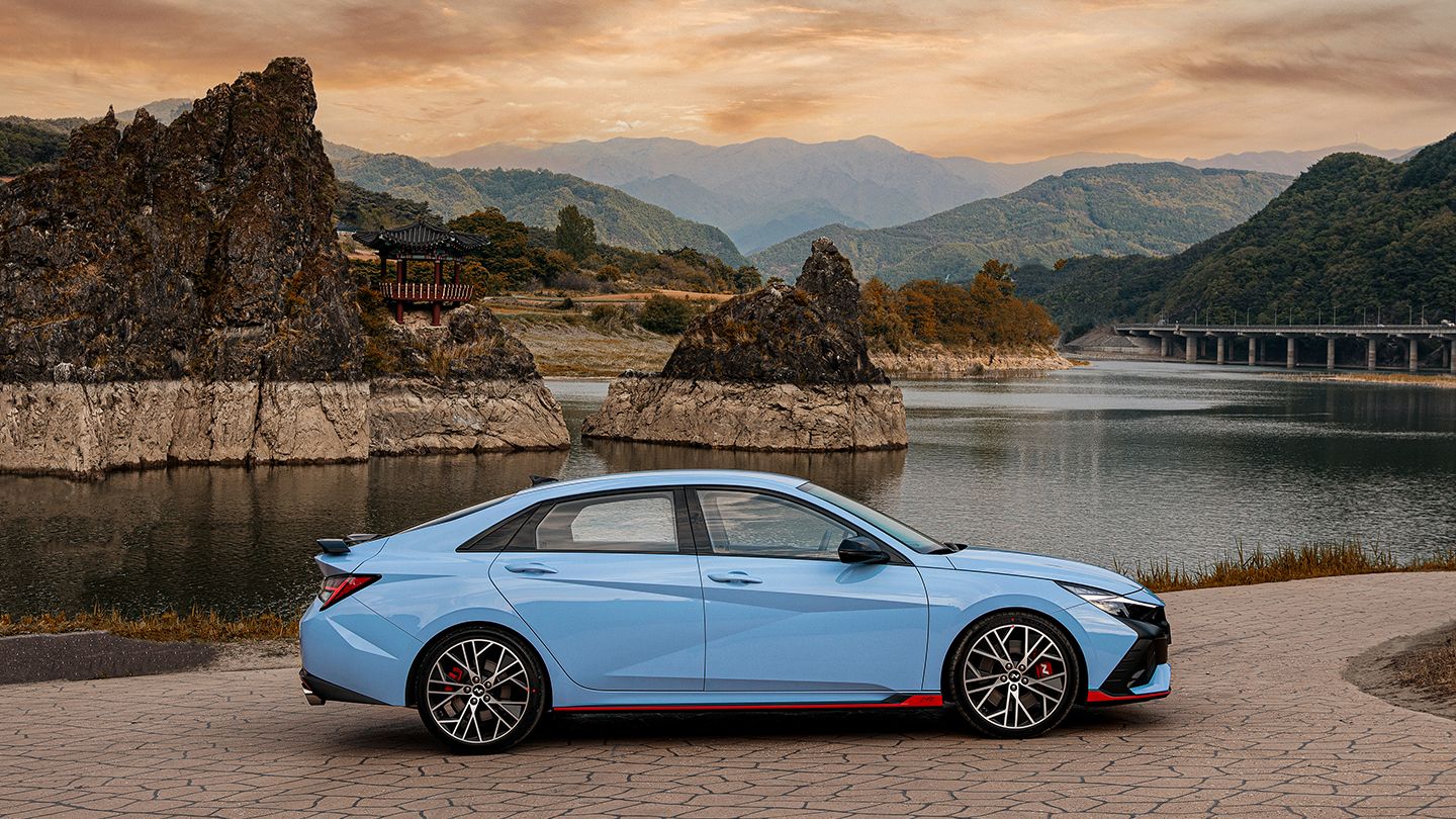 The mountains and river are visible in the background behind the Elantra N parked on the right.
