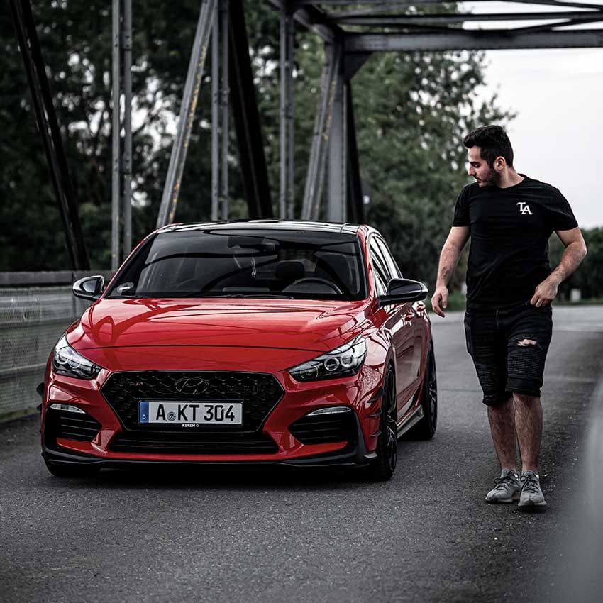 A man standing beside a parked i30 N, looking at the car.