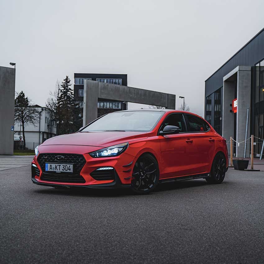 The side of the i30 N vehicle is seen parked in front of the building.