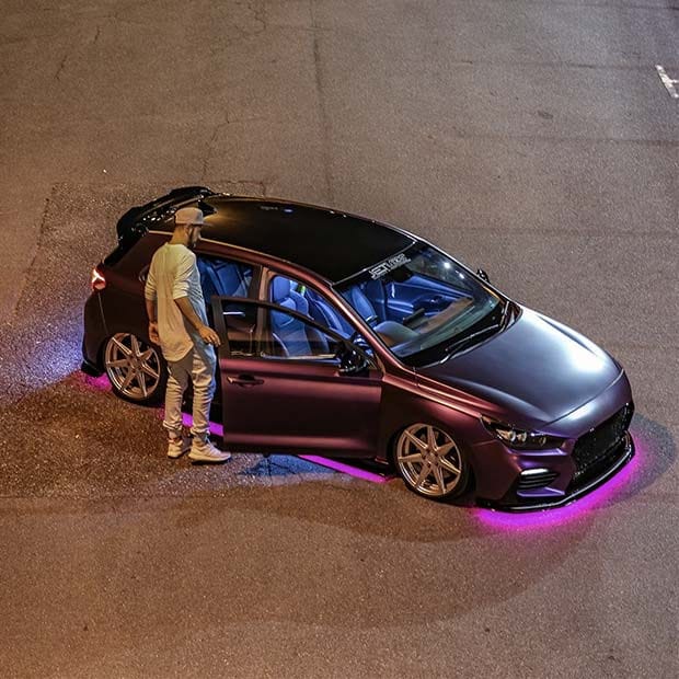 A man opening the passenger door of a parked car on the asphalt.