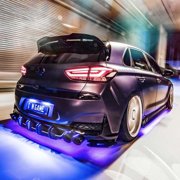 A vehicle is parked in a space illuminated by a neon sign. The rear of the vehicle is visible.