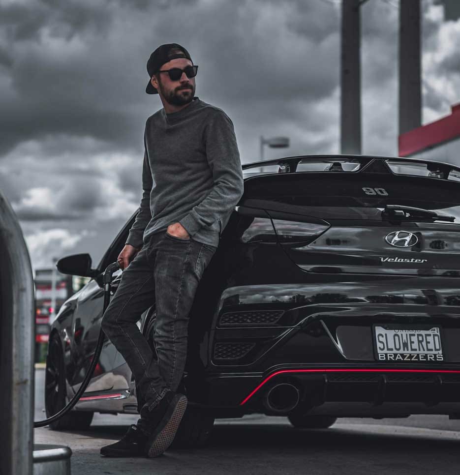 A man is seen filling up his Veloster N vehicle. He is wearing sunglasses and a hat.