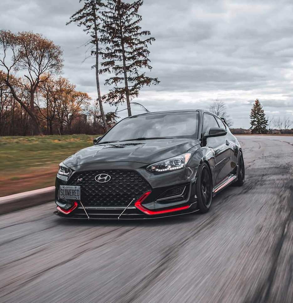 The front of a Veloster N vehicle is seen driving on a road next to a park.