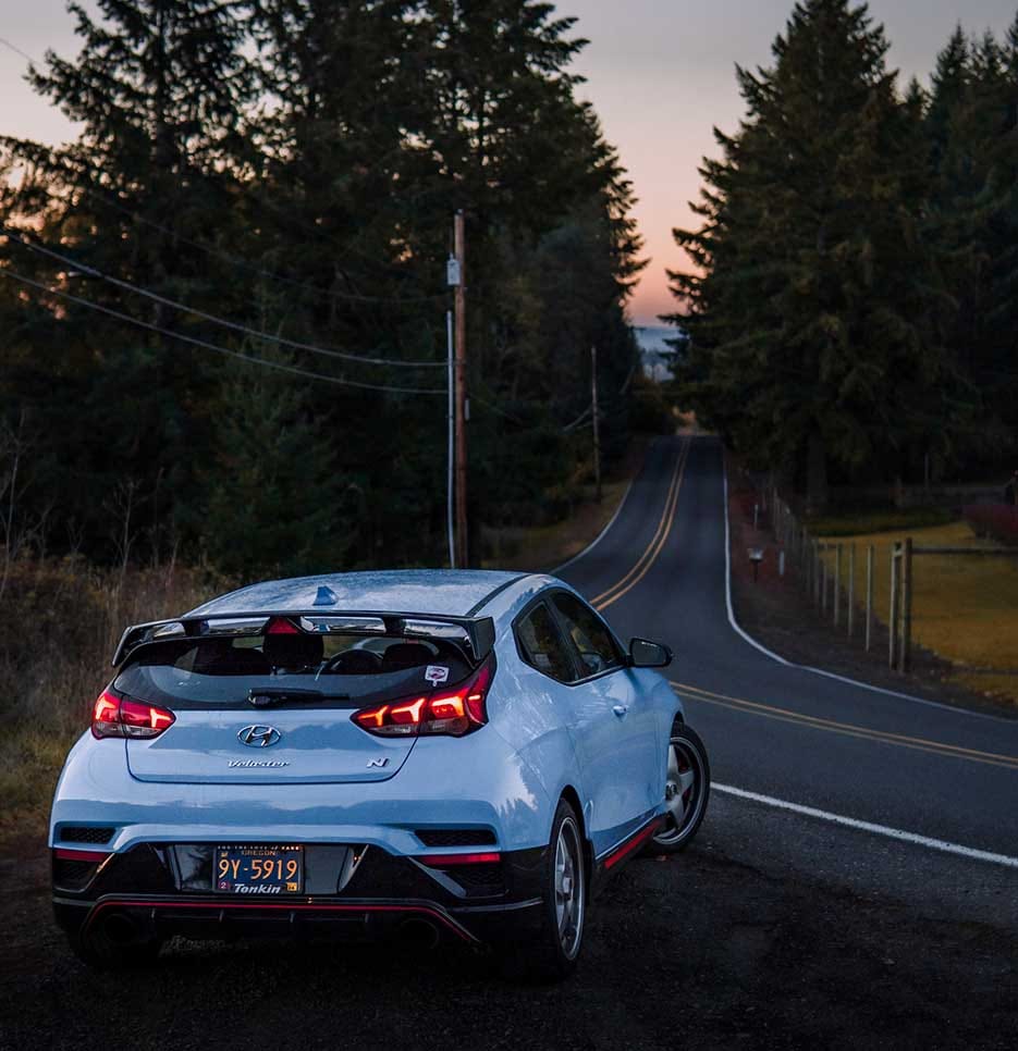 The sunset is visible ahead of a vehicle driving on a long forest road.