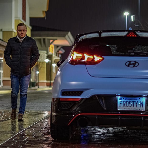 A man walking past a parked car with its rear lights on.