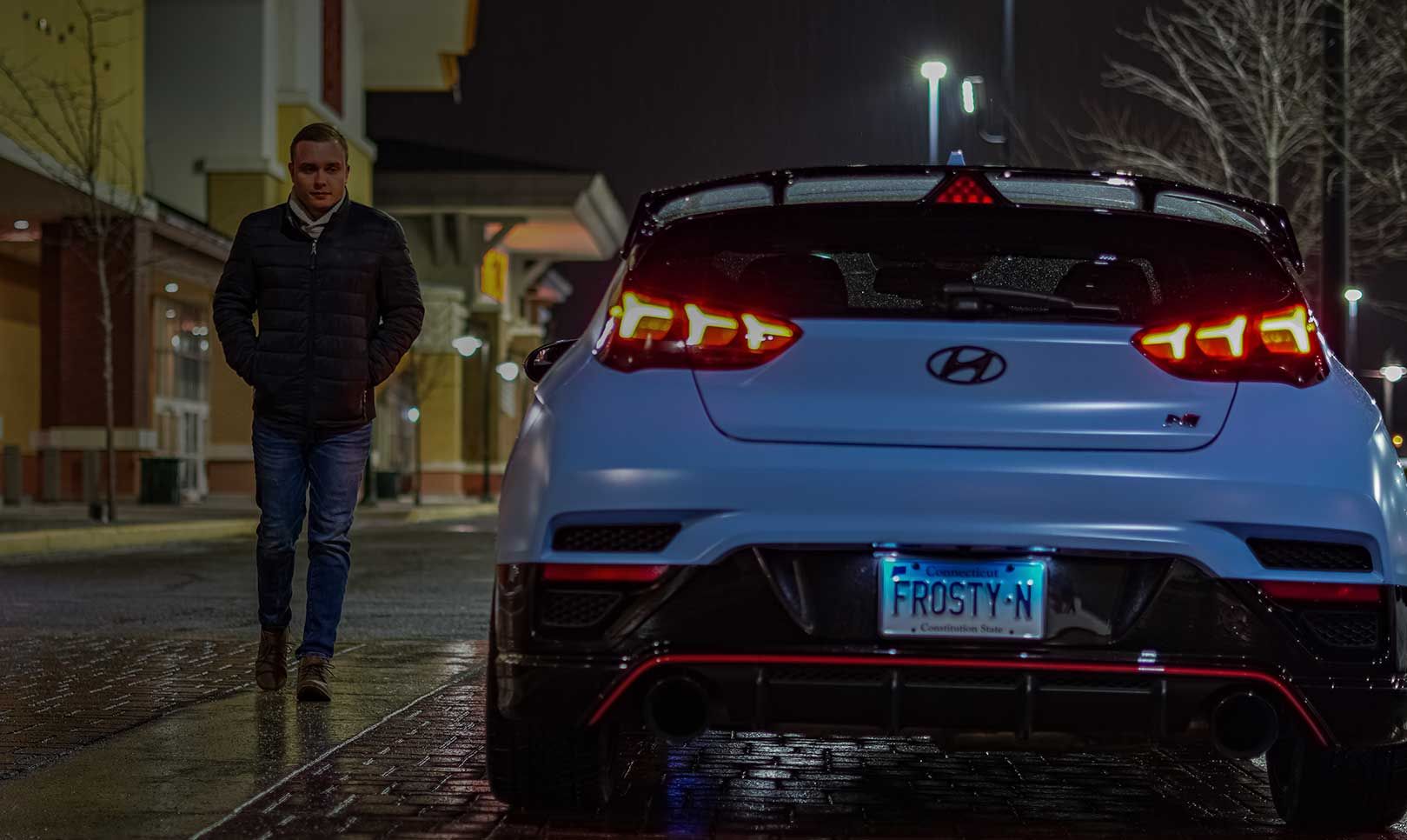 A man walking past a parked car with its rear lights on.