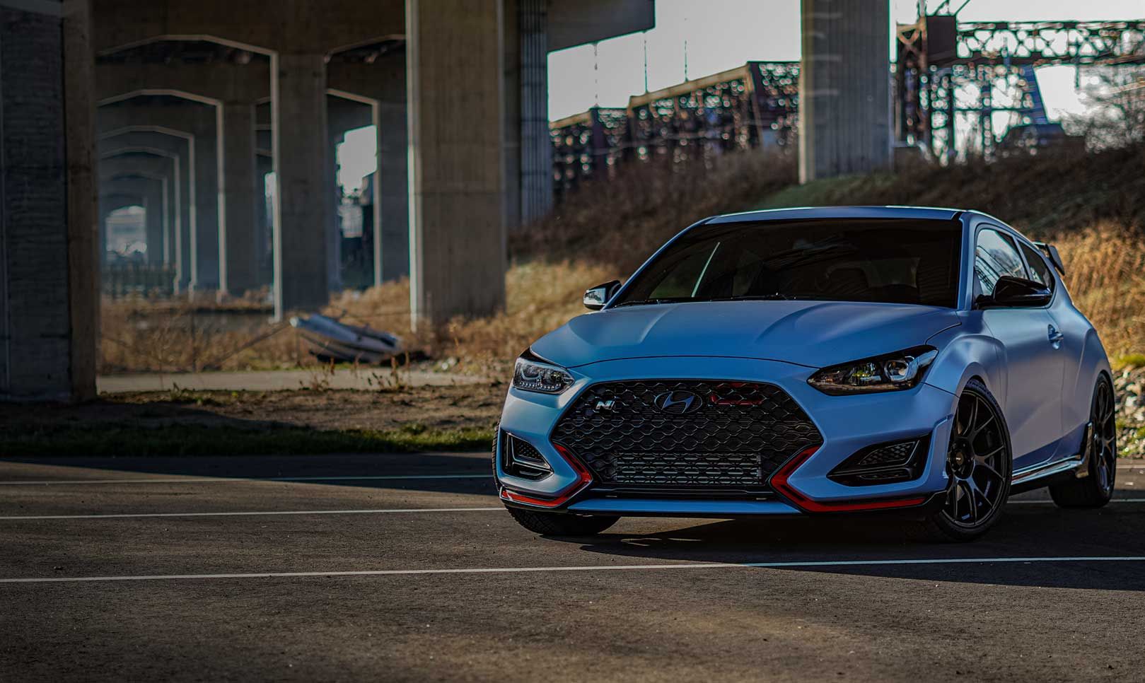 Reeds are visible behind the vehicle parked under the overpass.