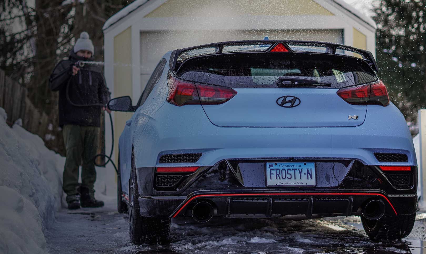 A man sprays water on a car on a snow-covered road.