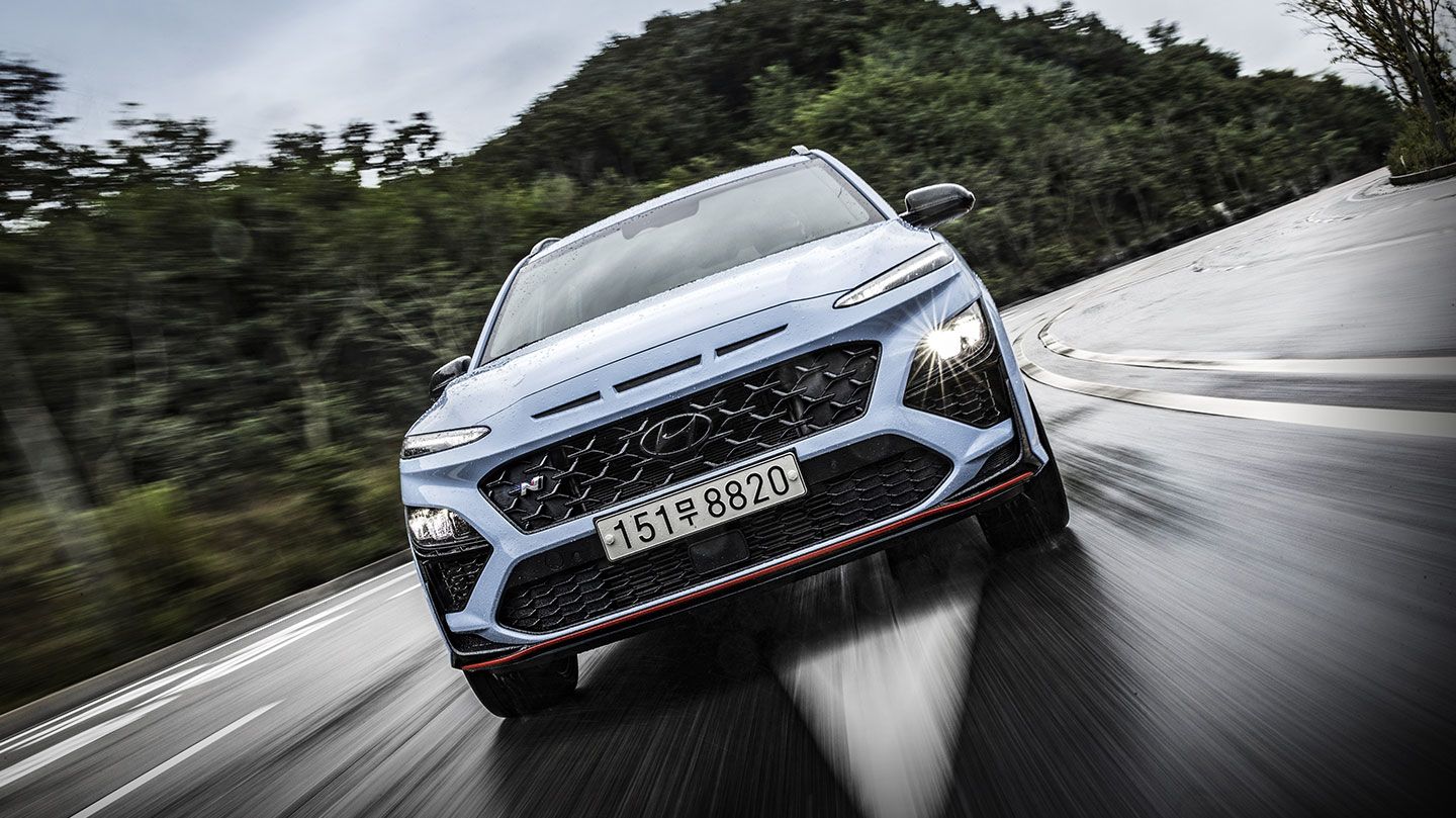 Kona N driving on the road with its headlights on.