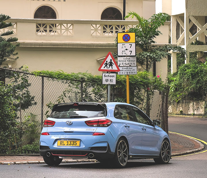 An i30 driving on a road in Hong Kong with vines. A road sign is visible