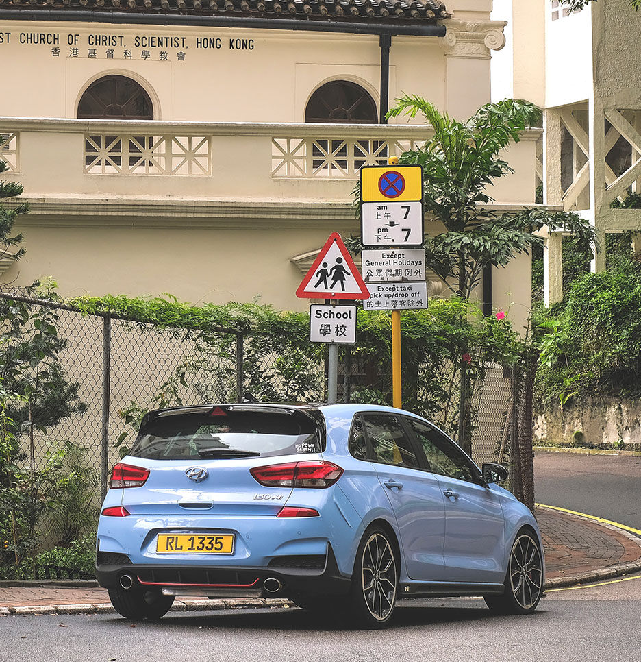 An i30 driving on a road in Hong Kong with vines. A road sign is visible