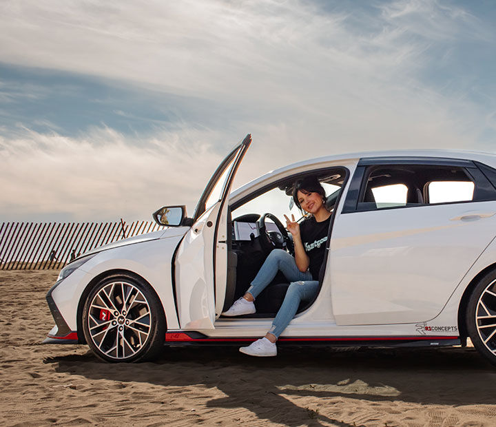 Nfluencer posing while sitting on the driver's seat with the car's door open