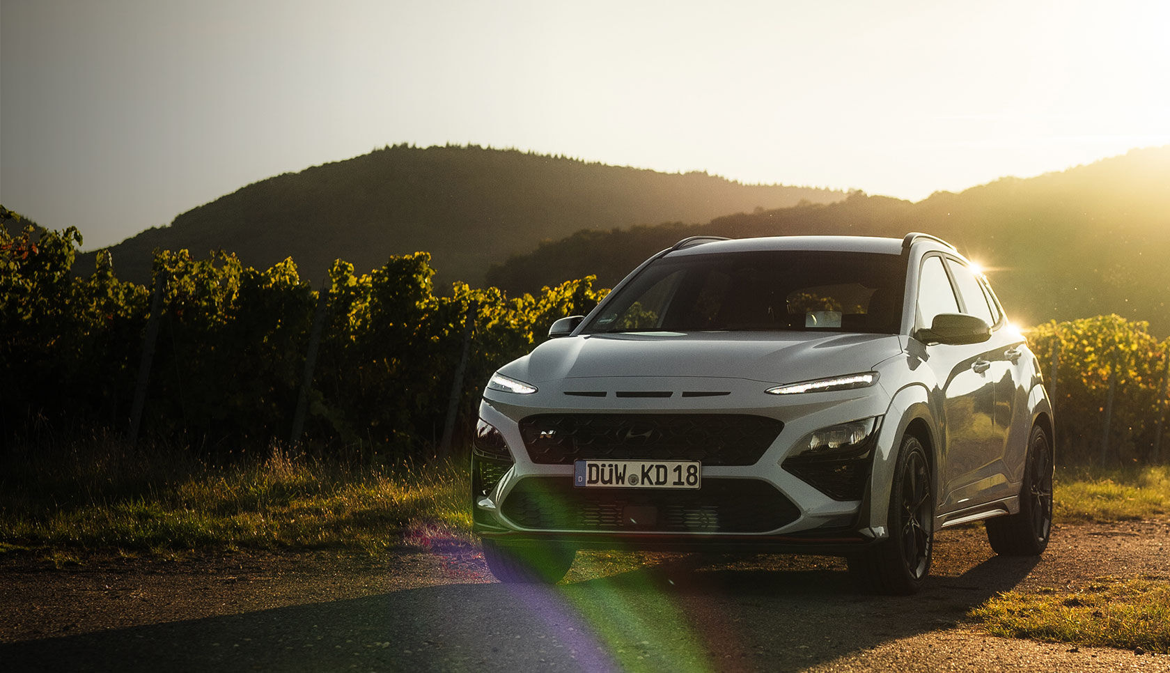 Sunlight shines behind a car parked in a field