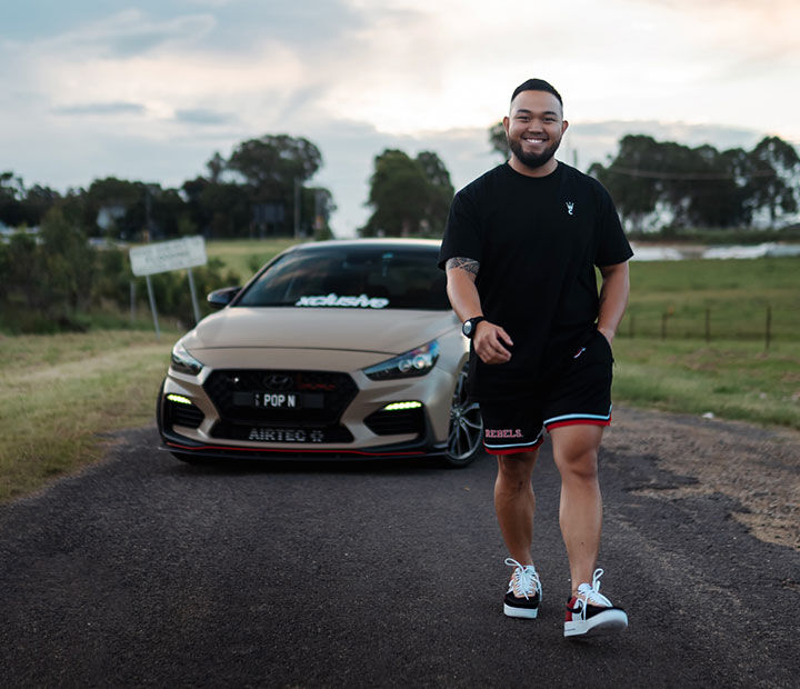 Nfluencer posing in front of a car parked on a quiet country road