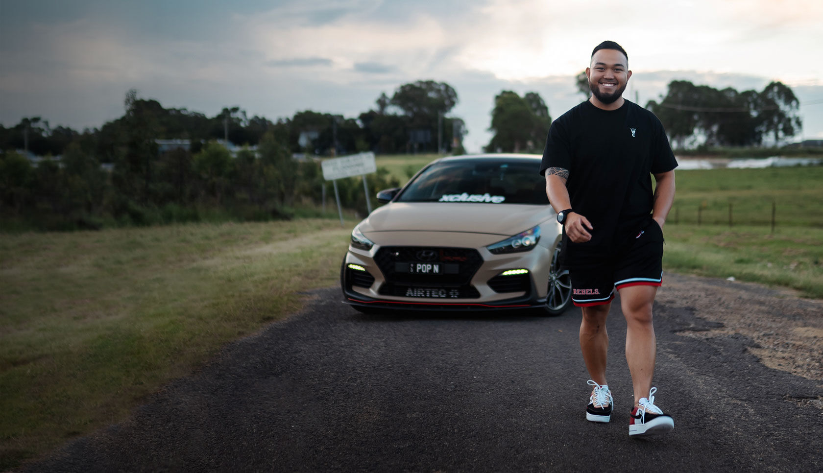 Nfluencer posing in front of a car parked on a quiet country road
