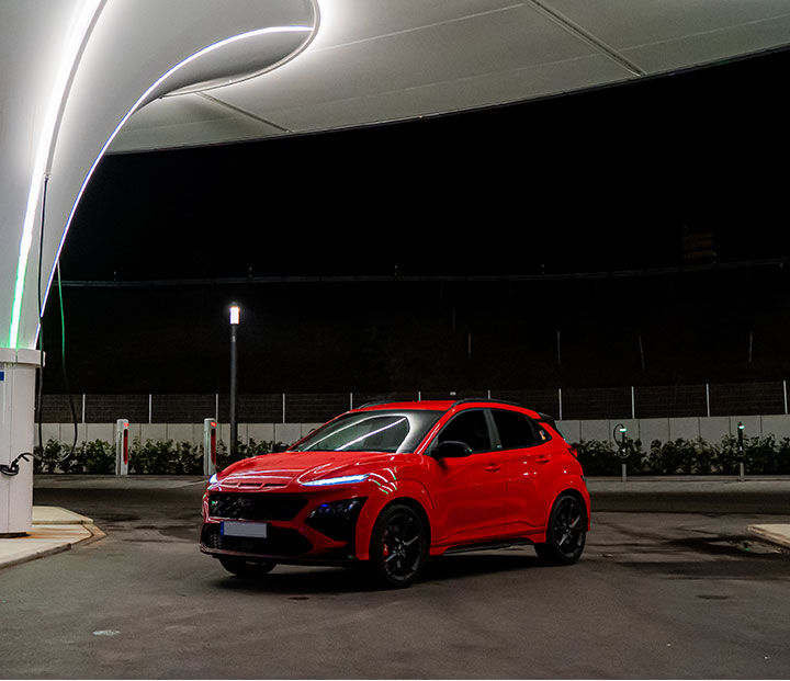 The front of a car is visible, parked in front of a building with lights on
